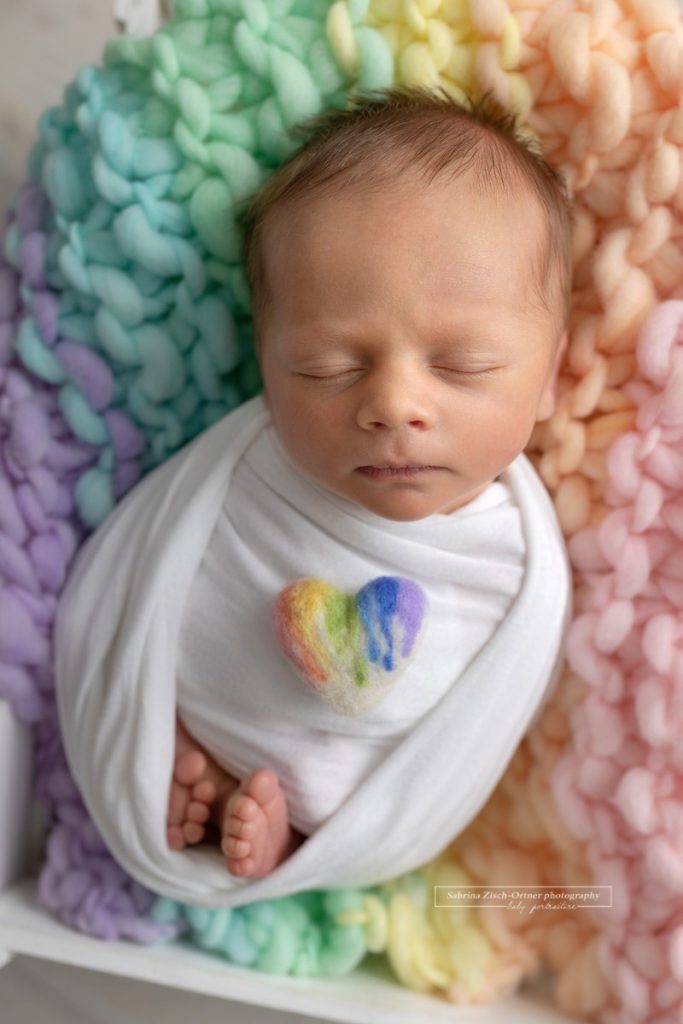 Neugeborenes Regenbogen Baby auf Decke mit Herzchen beim Shooting mit Sabrina Zisch Ortner
