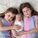 großen Schwestern in Regenbogenkleidern mit Baby