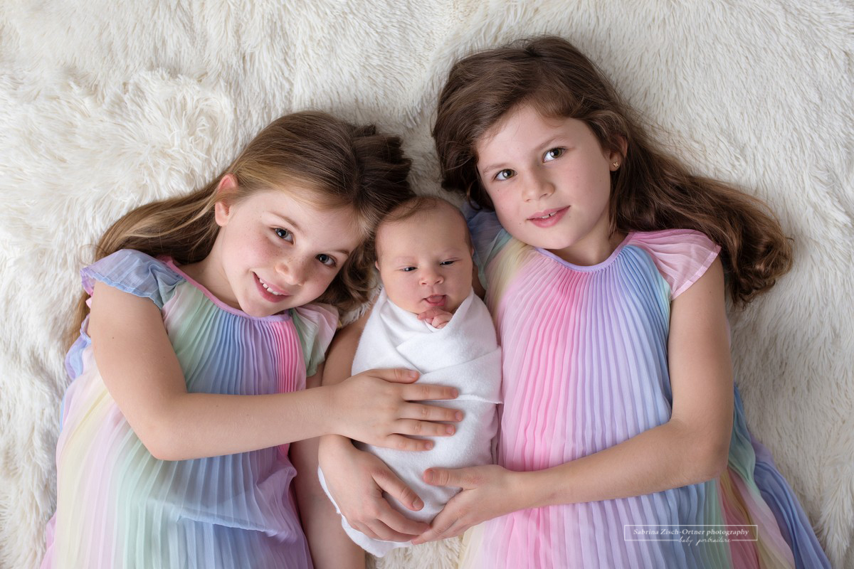 großen Schwestern in Regenbogenkleidern mit Baby