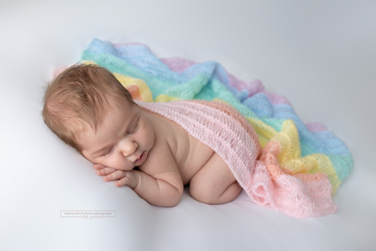 schlafendes Baby eingekuschelt in Regenbogen Decke