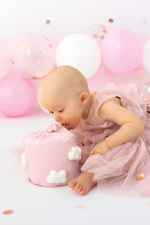 Baby wird ein Jahr alt mit Torte Luftballons und rosa Kleid