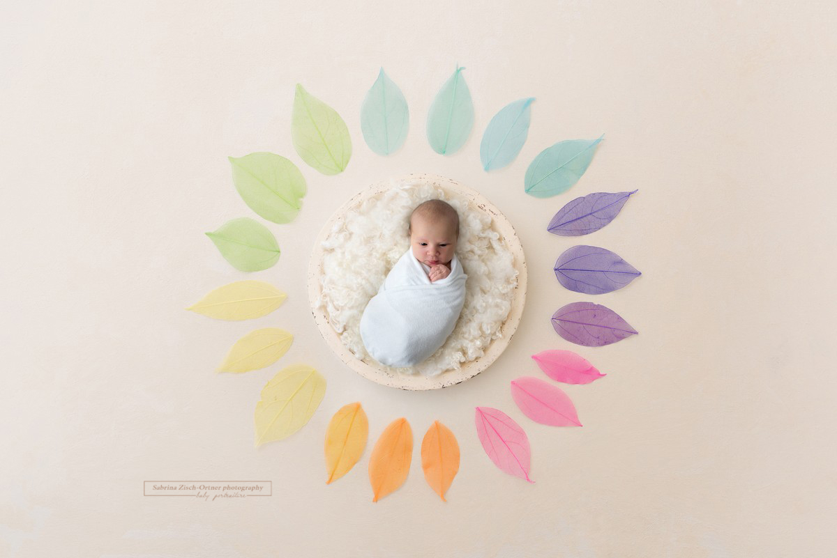 Baby umringt mit Blättern in Regenbogenfarben
